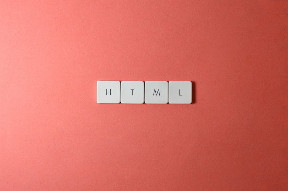 Four small white plastic tiles with black letters spelling 'H', 'T', 'M', and 'L' are arranged on a smooth, dark grey surface. The tiles are positioned in a loose cluster, with the 'H' and 'T' slightl